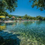 Découvrez le paradis caché du Jura : ce lac aux eaux turquoises va vous faire rêver Piscine naturelle entourée d'arbres sous un ciel bleu et ensoleillé