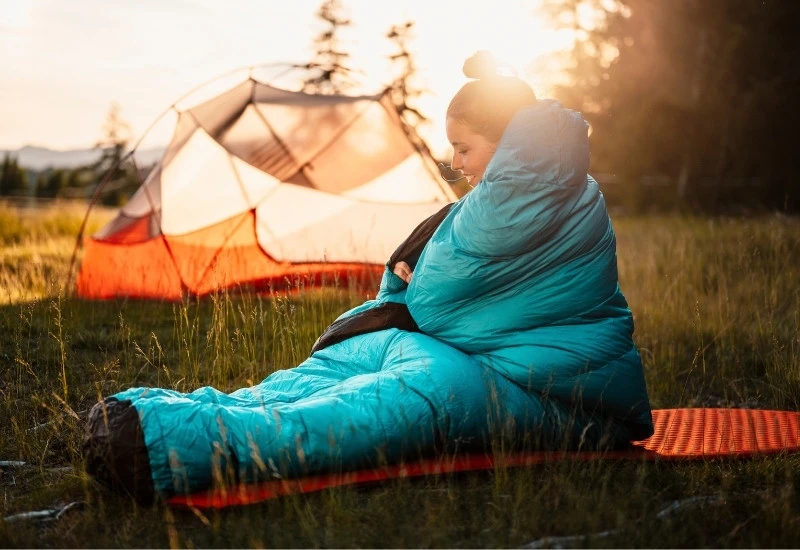 une femme dans un sac de couchage devant une tente