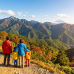 Famille de dos admirant un vaste paysage montagneux japonais en automne, avec le Mont Fuji enneigé à l'horizon.