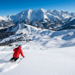 La station Clusaz : ski, massifs et activités au sommet Skieur en veste rouge sur une piste immaculée, avec les sommets enneigés et forêts des Alpes sous un ciel bleu clair.