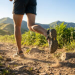 Coureur en sandales de trail sur un sentier montagneux, illustrant la foulée naturelle et l'agilité.