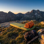 Matelas de bivouac et sac de couchage installés sur une crête rocheuse face à une chaîne de montagnes au lever du jour.