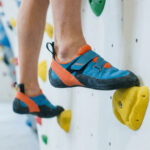 Gros plan sur les pieds d'un grimpeur posés sur des prises d'escalade colorées sur un mur en salle.