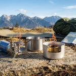 Réchaud à gaz ou à alcool : quel système pour le trek ? Un réchaud à gaz et un réchaud à alcool posés sur une roche en montagne avec un sac à dos et une carte.