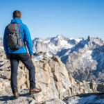 Un randonneur équipé d'un sac à dos regarde des sommets enneigés depuis le sommet d'une montagne.