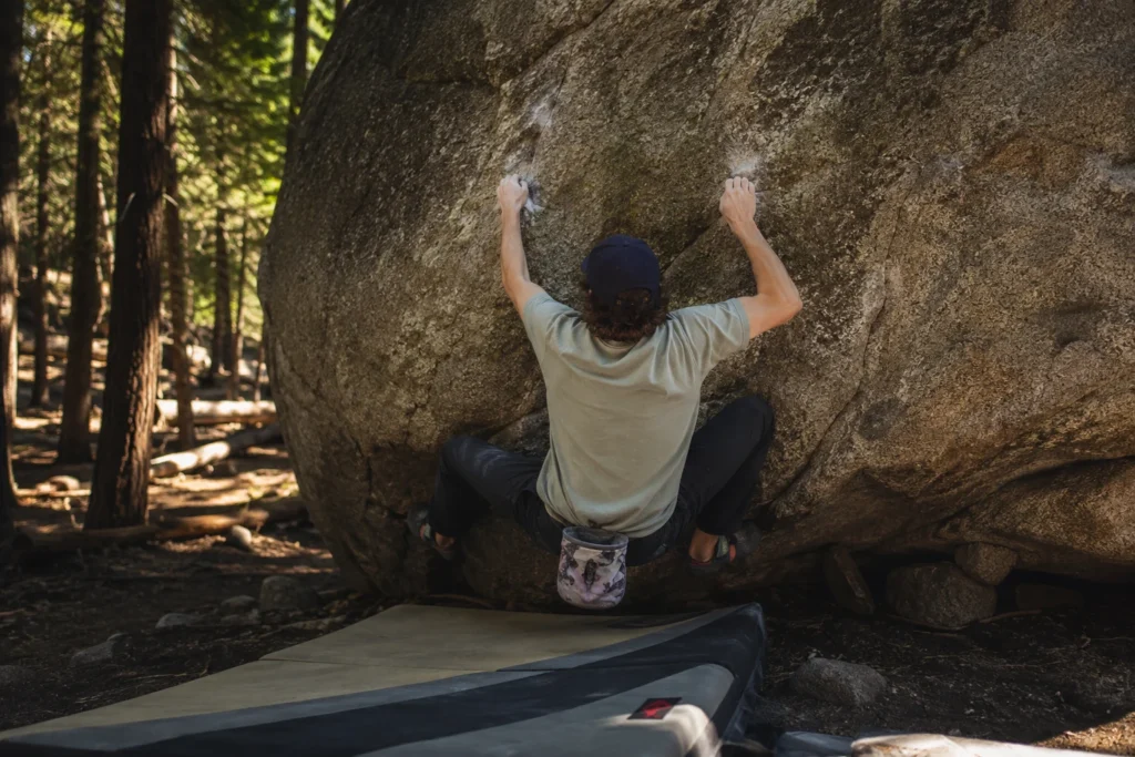 Grimpeur de bloc de dos accroupi sur un rocher en forêt, tapis de réception au sol