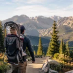 Randonneur vu de dos portant son enfant dans un porte-bébé sur un sentier de montagne.